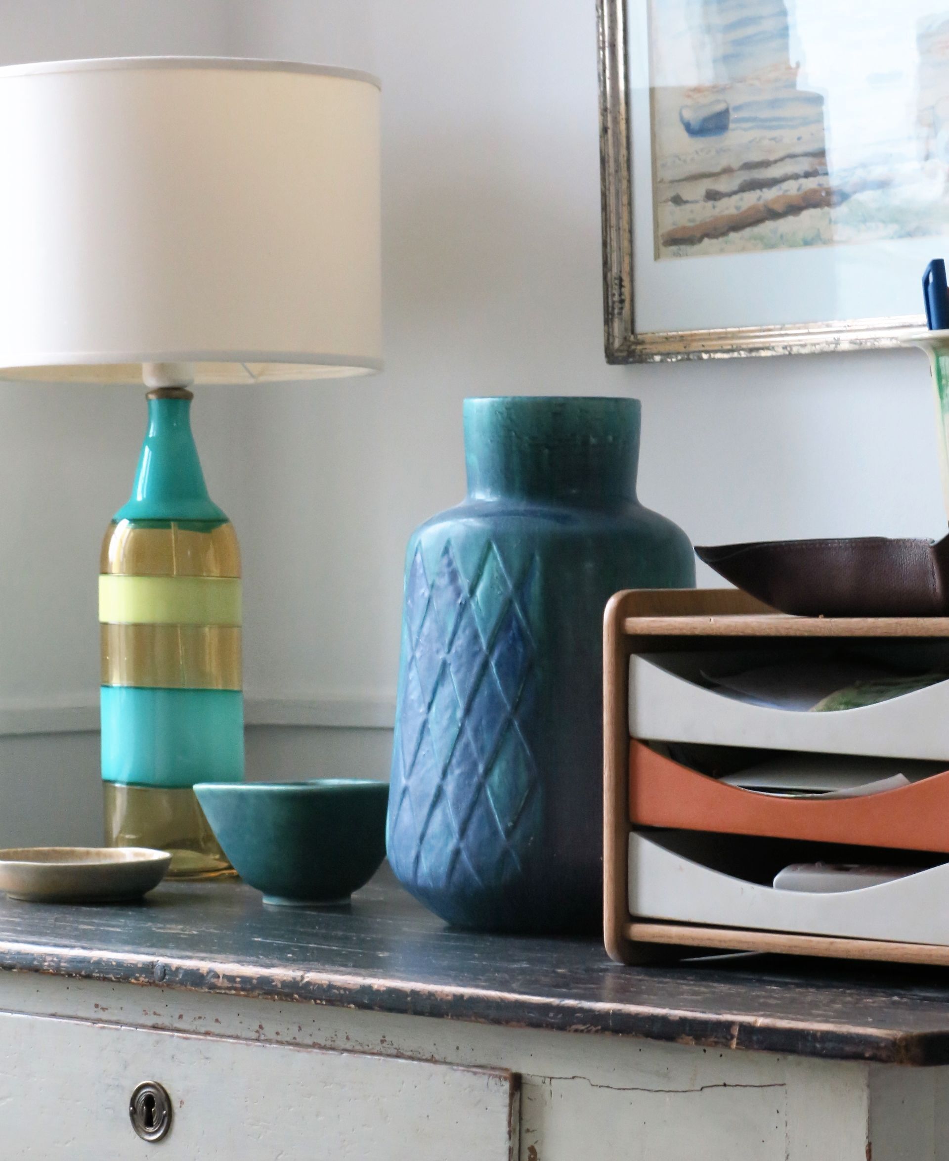 A table with a teal lamp, a blue vase, a teal bowl, and a brown tray with compartments.