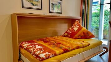 A bed with a wooden headboard, two framed pictures on the wall, and a window with curtains.