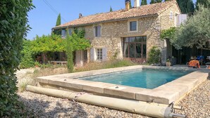 Une maison en pierre avec une piscine, entourée de gravier et de verdure.