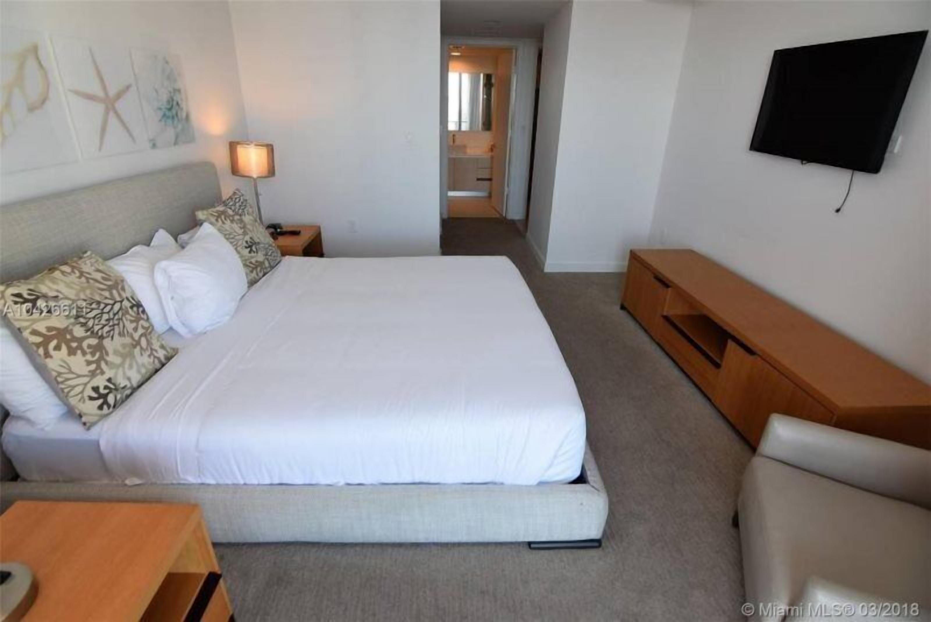 A hotel room with a large bed, a TV mounted on the wall, a wooden nightstand, and a small table.