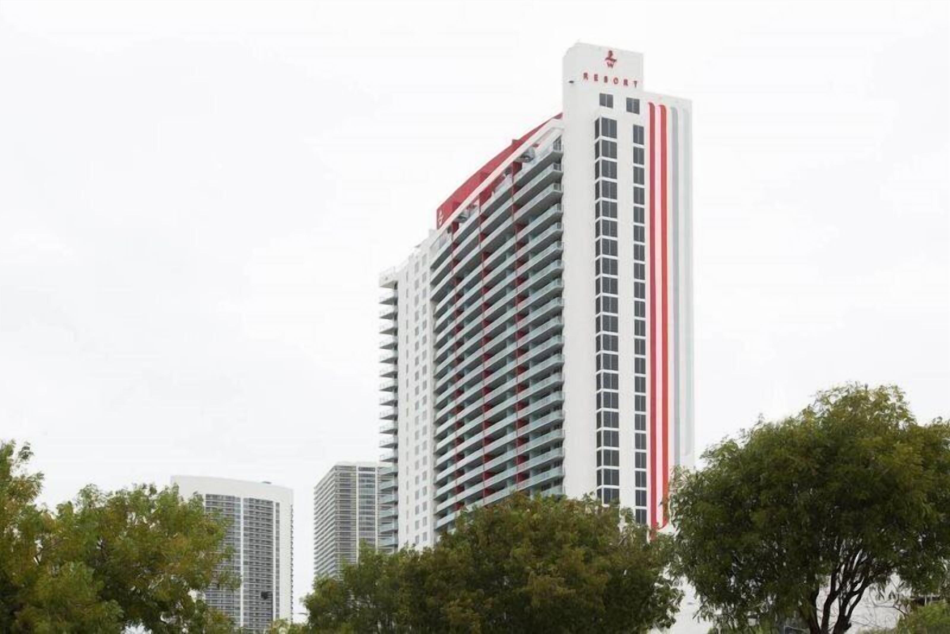A tall, modern hotel building with a red and white color scheme, featuring multiple balconies and a prominent signage at the top.