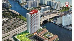 A high-rise hotel with a red roof, situated by a river with a bridge nearby.