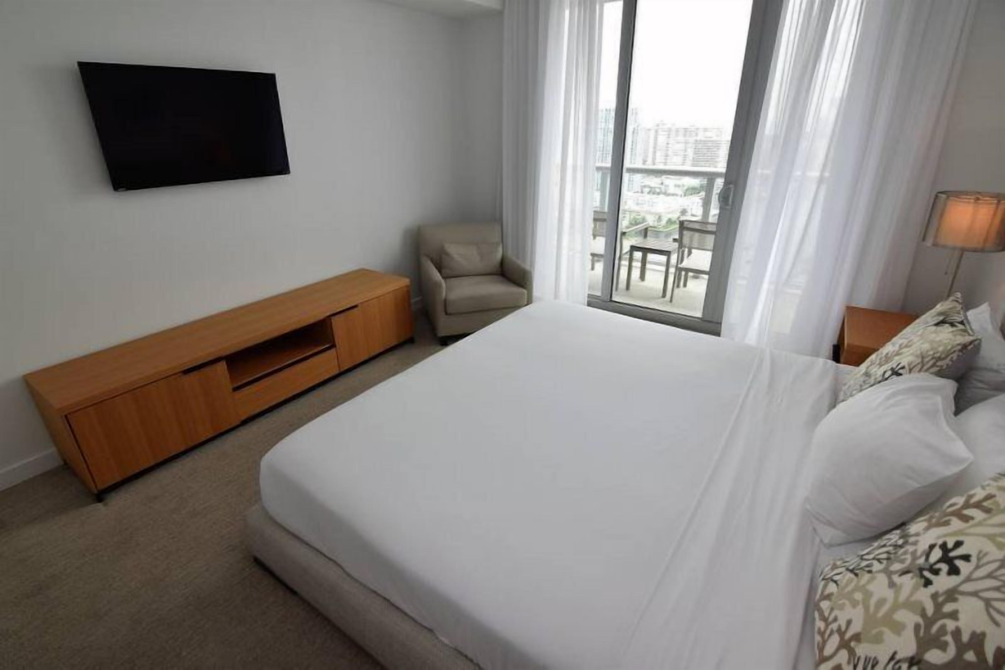 Ein Hotelzimmer mit Bett, Wandfernseher, Stuhl, kleinem Tisch und einem Balkon mit Stadtblick.
