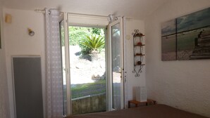 A bedroom with a bed, a sliding glass door to a garden, a small table with a lamp, and a wall-mounted shelf with decorative items. - 800m from the sea, pretty Provencal villa, quiet, swimming pool, garden in the Golf St. Tropez (Roquebrune-Sur-Argens)