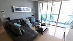 Una sala moderna con un amplio sofá seccional, una mesa de centro y un balcón con vistas a la ciudad.