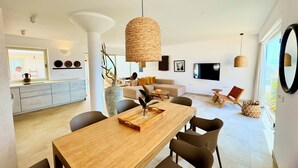 A modern living room with a large TV, a dining area with a wooden table, and a kitchen with a window. - Bungalow with private pool, internet, close to the sea, courtyard, top location, parking lot (Costa Calma)