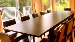 A conference room with a long table and chairs, large windows with a view of trees, and a white railing outside. - Family home in Surrey (Surrey)