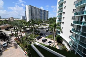 A high-rise hotel with multiple floors, a parking area with several cars, and palm trees. - Tides-5q (Hollywood)