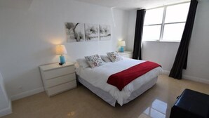Ein Schlafzimmer mit einem großen Bett, weißen Nachttischen, einer roten Tagesdecke und Kunstwerken an der Wand.