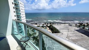 Ein Balkon mit Glasgeländer, der Blick auf Strand und Meer freigibt.