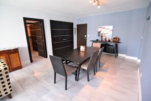A modern dining area with a dark wooden table and chairs, a small decorative centerpiece, and a kitchen area in the background.