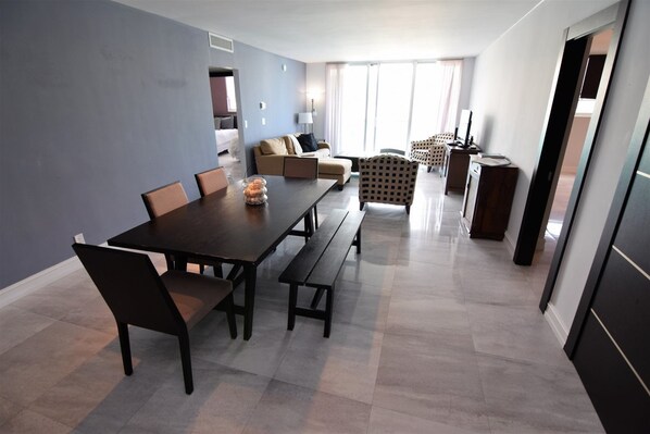 A modern living room with a dark wooden dining table, comfortable seating, and a large window providing natural light.