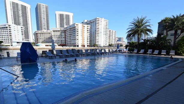 A swimming pool with lounge chairs and a cityscape in the background. - Ocean & Bay View Residence 1 Bed 1 Bath @ Beachwalk Hallandale Beach (Hallandale Beach)
