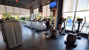 A gym with treadmills, weight machines, and a large window with a view of buildings. - Ocean & Bay View Residence 1 Bed 1 Bath @ Beachwalk Hallandale Beach (Hallandale Beach)