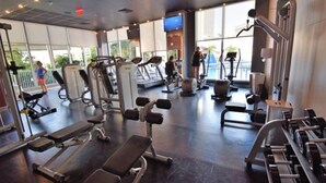 Un gimnasio con diversos equipos de ejercicio, ventanas amplias y vistas al exterior.