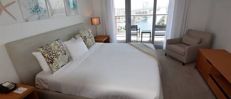 A hotel room with a large bed, a desk, a chair, and a view of the city through the window.