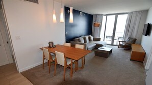 Ein modernes Wohnzimmer mit einem Holzesstisch, beigen Sofas und einem großen Fenster mit Vorhängen.