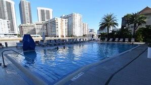 Ein Schwimmbecken mit Liegestühlen und einer Stadtkulisse im Hintergrund.