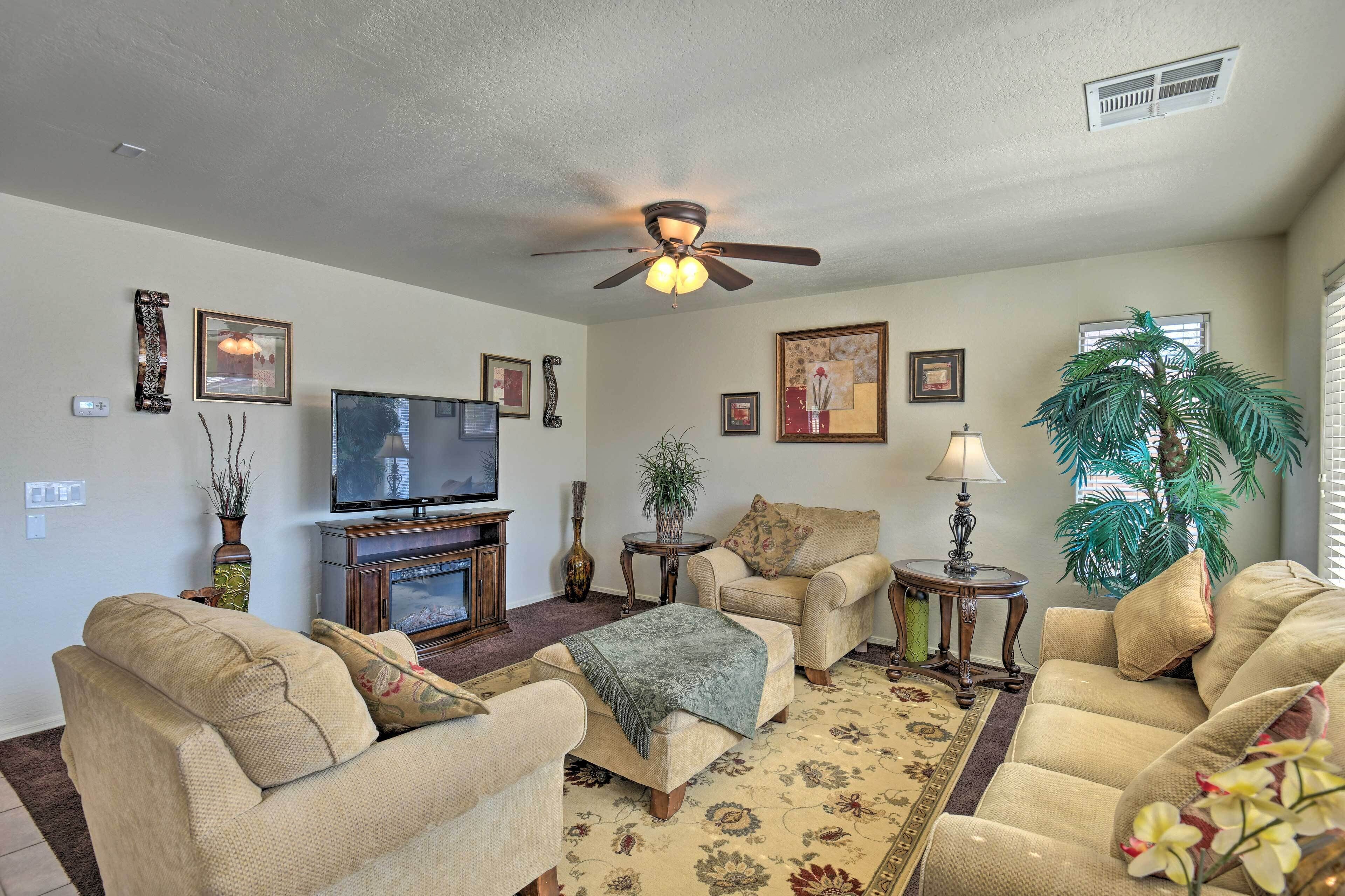 A living room with a ceiling fan, a television, a fireplace, and a large plant.