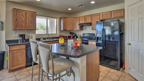 A kitchen with wooden cabinets, a central island with chairs, a refrigerator, and a stove. - Relaxing San Tan Valley Retreat w/ Pool & Hot Tub! (San Tan Valley)