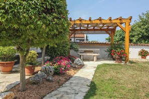Um jardim com pérgola, vasos de plantas, caminho de pedra e um banco de pedra.