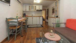 A compact kitchen with wooden cabinets, a dining table with chairs, and a sofa.