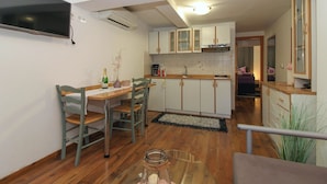 A compact kitchen with white cabinets, a dining area with a wooden table and chairs, and a TV mounted on the wall.