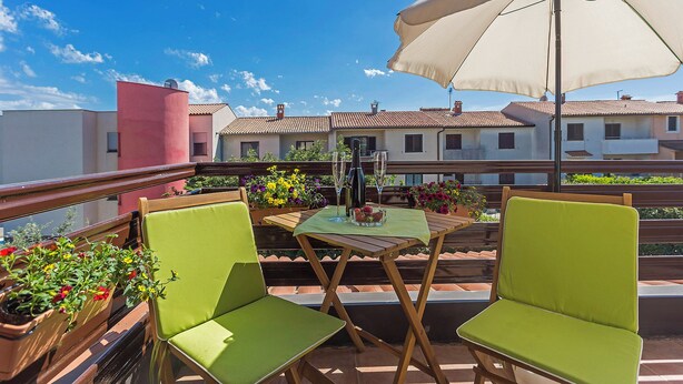 Un balcon avec deux chaises vertes, une table recouverte d’une nappe blanche et un grand parasol.