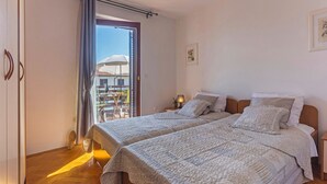 Une chambre avec deux lits, un balcon avec une table et un parasol, et une vue sur les bâtiments environnants.