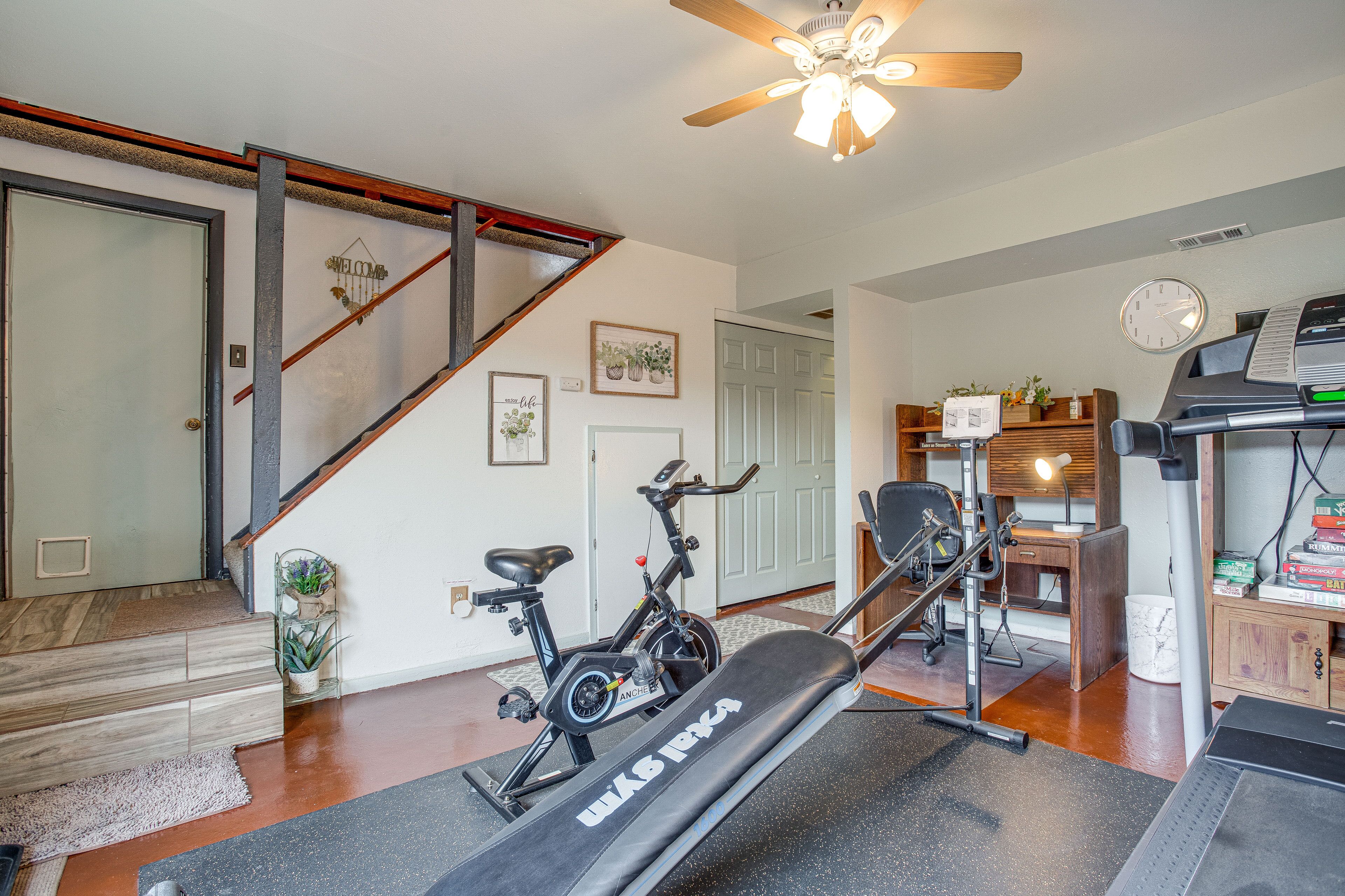 A home gym with exercise equipment, a staircase, and a living area with a desk and computer.