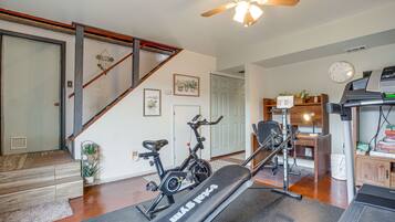 A home gym with exercise equipment, a staircase, and a living area with a desk and computer.