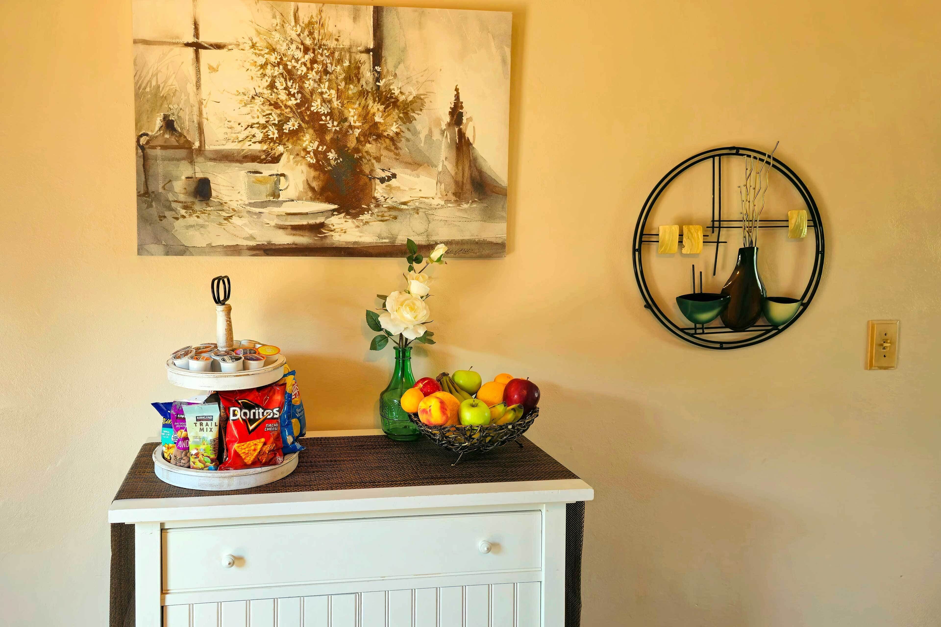 A kitchen counter with a jar of Doritos, a vase with flowers, and a fruit bowl.