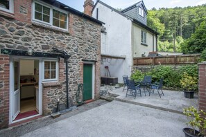 A stone building with a green door and a small outdoor seating area with chairs. - Robins Brook, Porlock (Porlock)