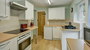 A compact kitchen with white cabinets, a built-in oven, a toaster, and a dishwasher. - Robins Brook, Porlock (Porlock)
