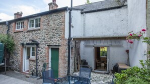 A stone building with a green door, a small patio with a glass table and chairs, and a wooden ladder leaning against the wall. - Robins Brook, Porlock (Porlock)
