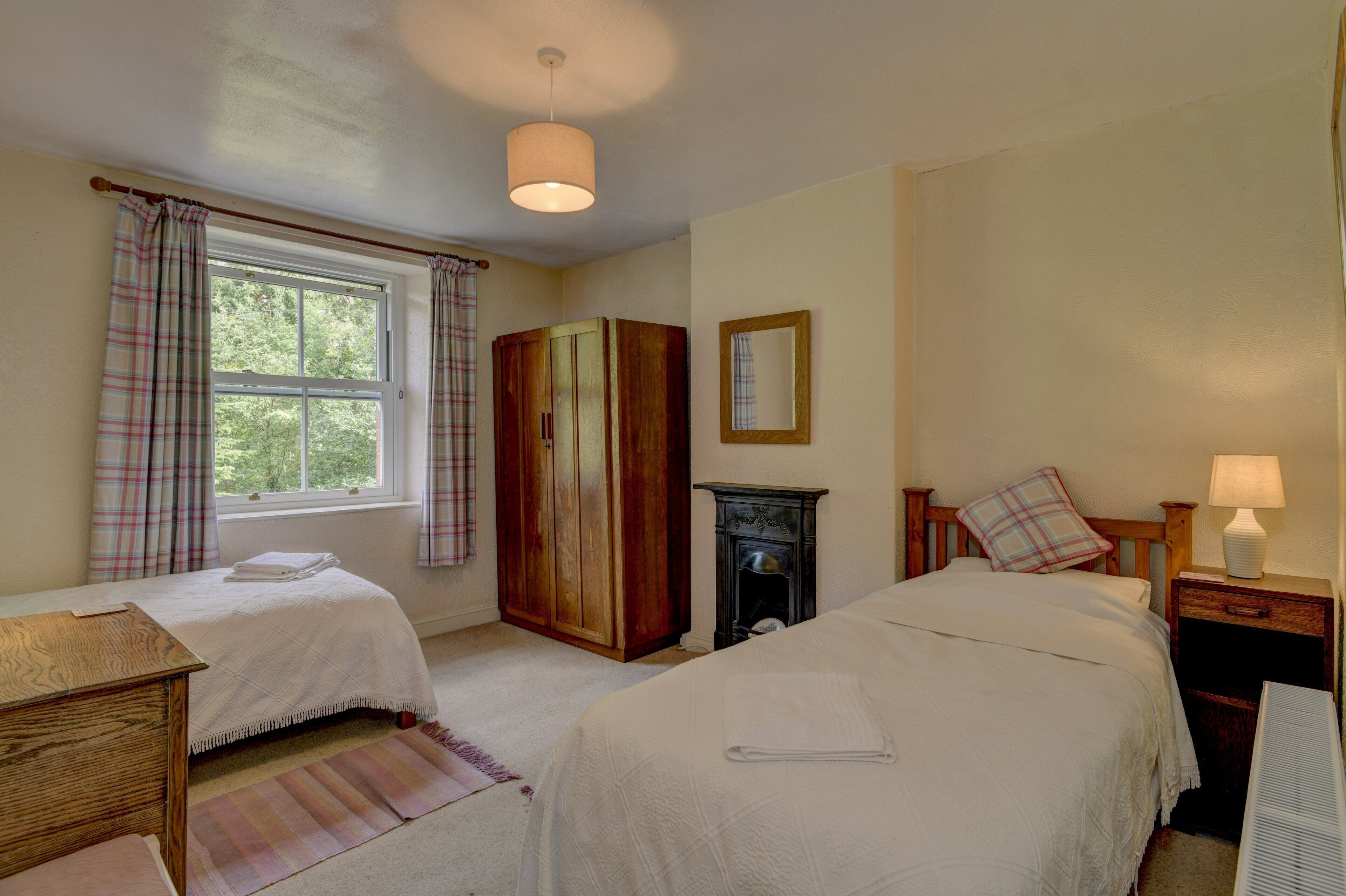 A bedroom with two beds, a wooden wardrobe, a fireplace, and a window with curtains.