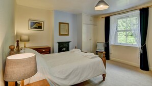 A bedroom with a bed, a nightstand, a lamp, a dresser, a mirror, a fireplace, and a window with curtains. - Robins Brook, Porlock (Porlock)