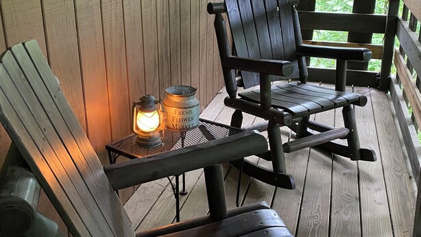 Un porche de madera con dos sillas Adirondack, una mesita con un farol y un cartel que dice 'Welcome'.