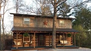 Una cabaña rústica de troncos con un porche, dos ventanas y una decoración con estrellas.