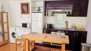 A compact kitchen with a washing machine, microwave, and a small dining table. - Beautiful River-front Apartment with Natural Pool (Sorède)