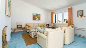 A living room with a sofa set, a television, a fireplace, and a window with curtains. - Liiiving in Algarve | Alvor Blue Villa (Alvor)