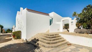 A white building with a red-tiled roof, a set of concrete steps leading to a door, and a clear blue sky in the background. - Liiiving in Algarve | Alvor Blue Villa (Alvor)