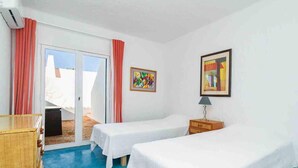 A room with two single beds, a wooden dresser, a small table with a lamp, and two framed artworks on the wall. - Liiiving in Algarve | Alvor Blue Villa (Alvor)