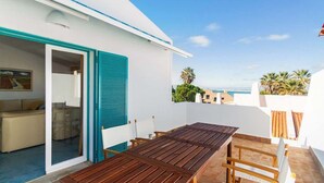 A balcony with a wooden table and chairs, a white building with teal shutters, and a view of the sea. - Liiiving in Algarve | Alvor Blue Villa (Alvor)