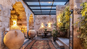 A courtyard with stone walls, a glass ceiling, and a central seating area with a table and chairs. - Carus Cappadocia (Nevsehir)