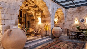 An interior with stone arches, a patterned rug, and a table with chairs. - Carus Cappadocia (Nevsehir)