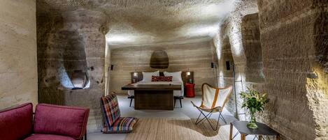 A bedroom with a stone ceiling, a bed, a red sofa, a chair, a small table with a vase, and a rug.