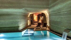An indoor swimming pool with clear water, surrounded by textured walls, and two lounge chairs. - Carus Cappadocia (Nevsehir)