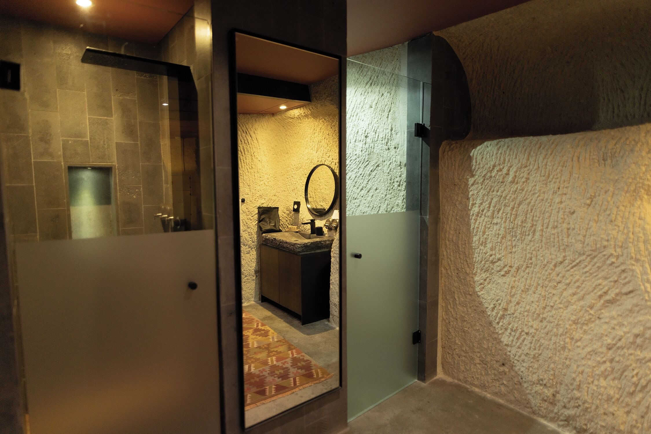 An interior view of a hotel room with a bathroom featuring a sink, mirror, and a textured wall.