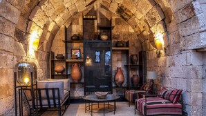 An arched stone room with a fireplace, shelves with pottery, a sofa, and a table. - Carus Cappadocia (Nevsehir)